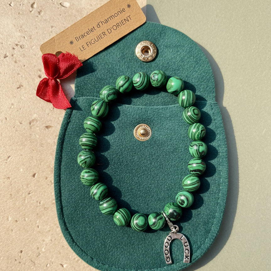 Bracelet d’harmonie en perles naturelles de malachite verte, orné d’un petit bijou symbolique et présenté dans une trousse en velours avec étiquette Le Figuier d’Orient.