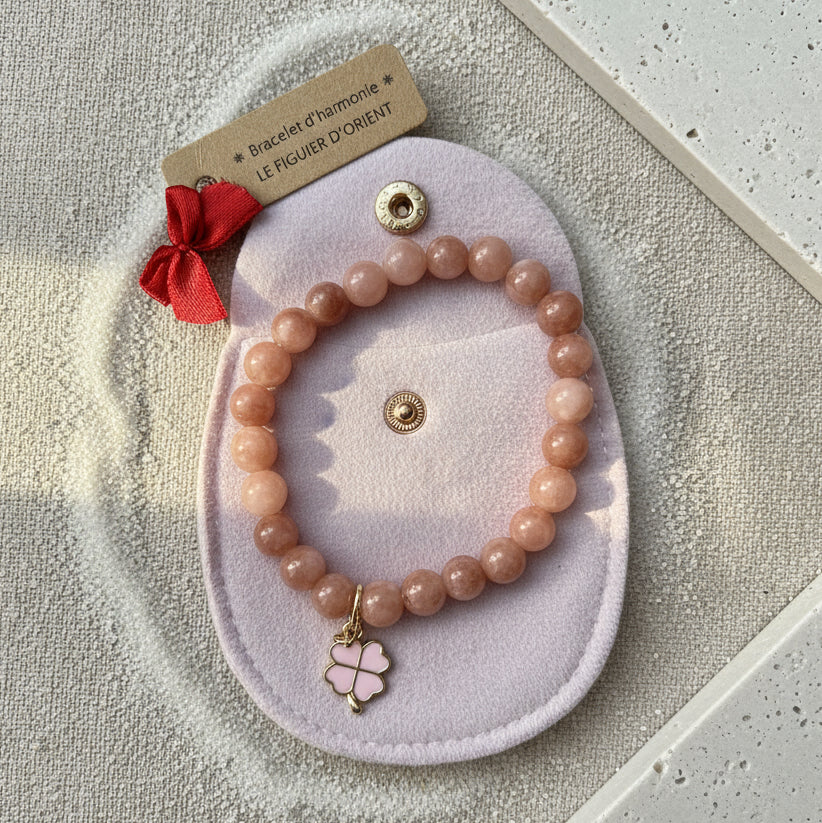 Bracelet d’harmonie en pierres naturelles de quartz rose, orné d’un pendentif trèfle porte-bonheur doré et présenté dans une trousse en velours rose, création artisanale Le Figuier d’Orient.