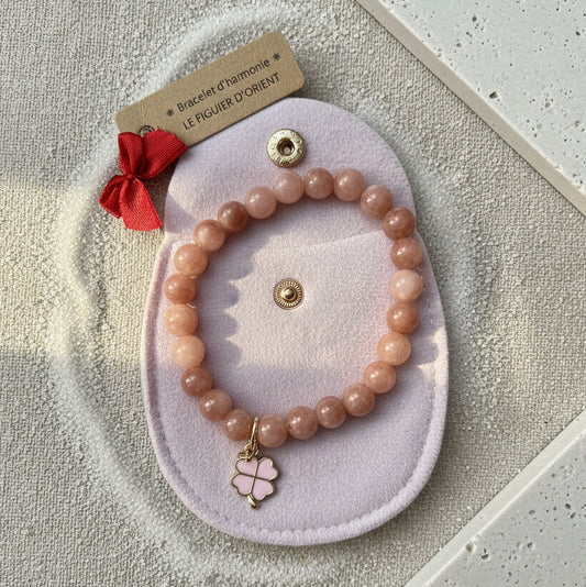 Bracelet d’harmonie en pierres naturelles de quartz rose, orné d’un pendentif trèfle porte-bonheur doré et présenté dans une trousse en velours rose, création artisanale Le Figuier d’Orient.