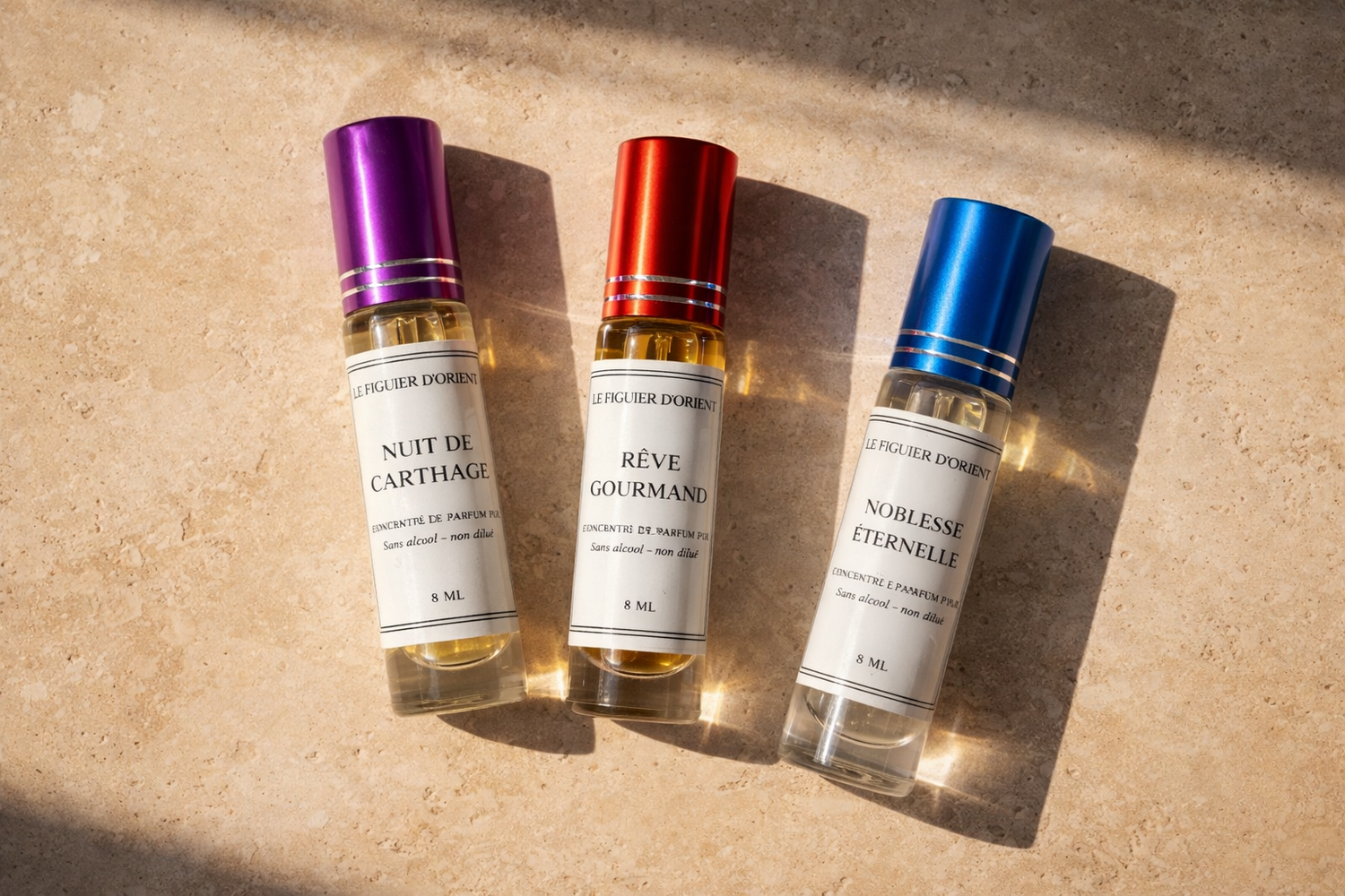 Muscs concentrés sans alcool Le Figuier d’Orient : Nuit de Carthage, Rêve Gourmand et Noblesse Éternelle, parfums orientaux naturels présentés sur fond marbre sable